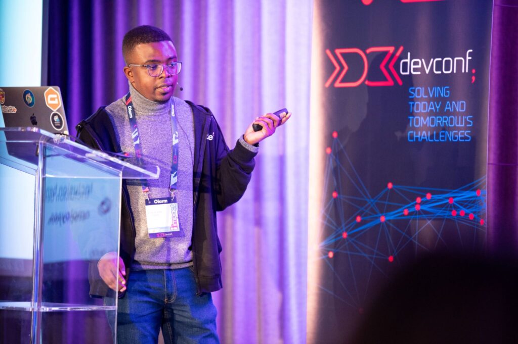 A pic taken of me while I was speaking at DevConf ZA 2025. I have a blue jean pants on, turtle neck top, and a hoodie.